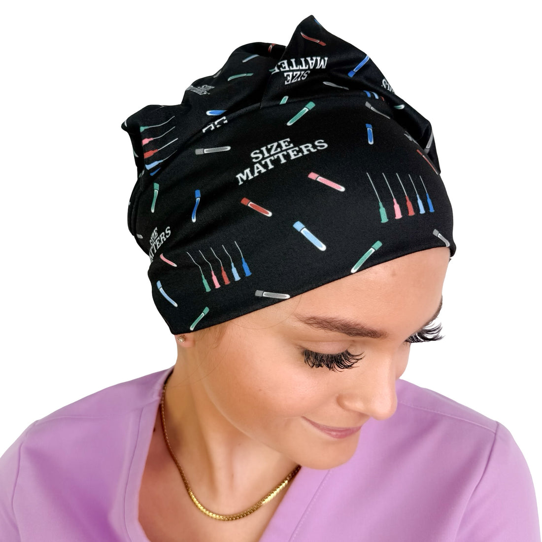 A woman wearing a black fabric SCRUB CAP  or surgical cap with a colorful needle and text pattern reading &